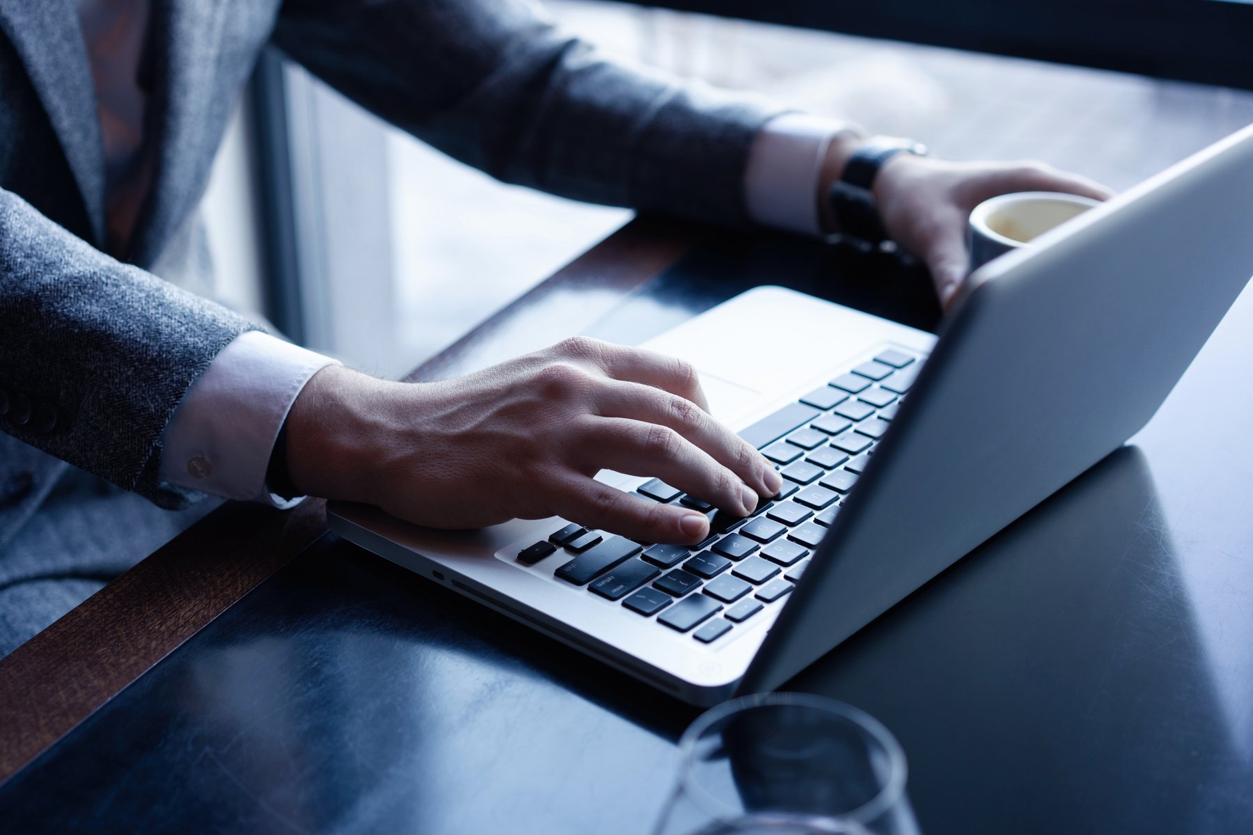 Young Man Working on His Laptop in a Coffee Shop, Rear View of Business Man Hands Busy Using Laptop at Office Desk.